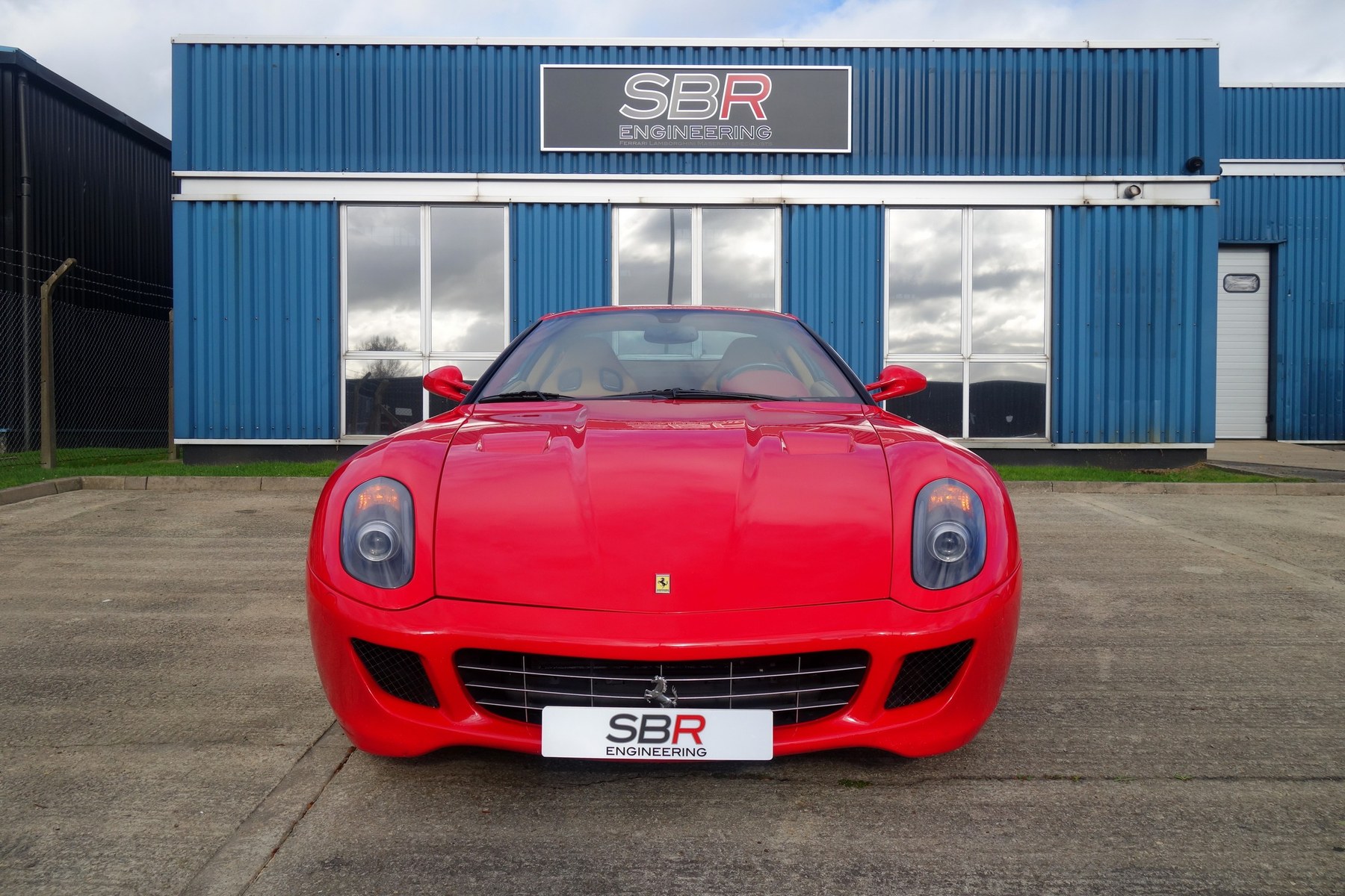 A red Ferrari 599 GTO parked outside the blue clad SBR Engineering unit in Aylesbury with the SBR Engineering sign above the door