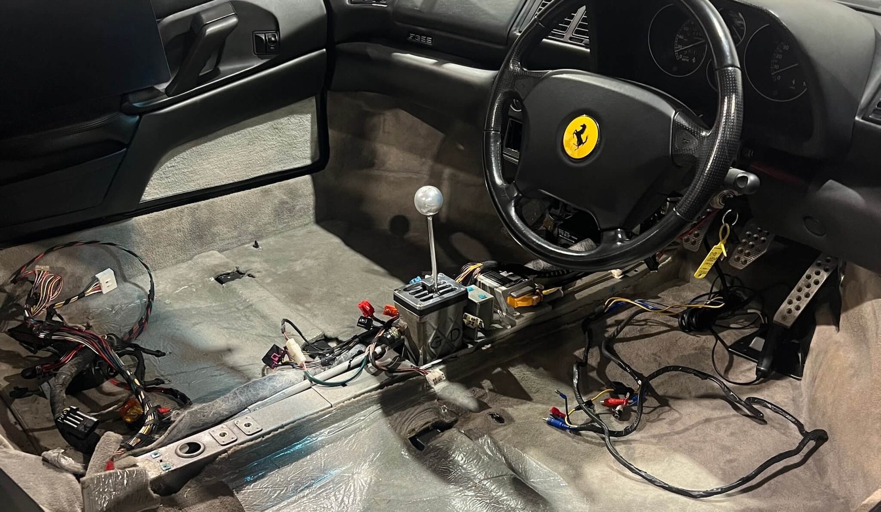 The interior of a Ferrari F355 stripped to the floor during a manual gearbox conversion, with the new gated shifter fitted and wiring exposed